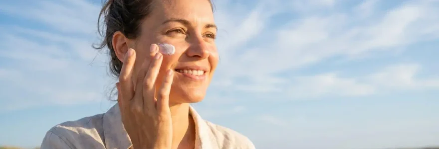 Femme appliquant une crème solaire SPF 50+ sur son visage en plein air, ciel bleu en arrière-plan